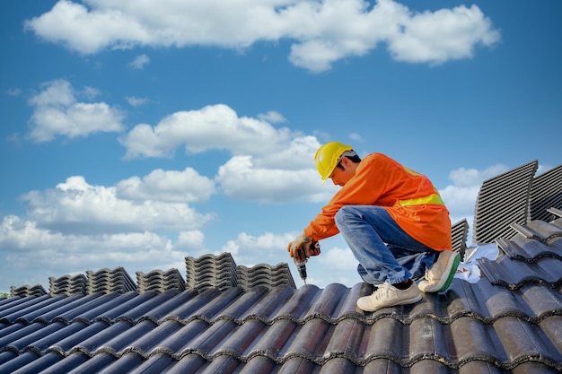 A male roofing installer is working on the roof of a house Construction workers repair the roof of a house using drills and screws