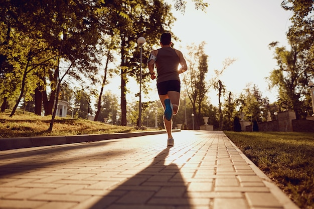 A male runner is running down the road in the park at sunset.