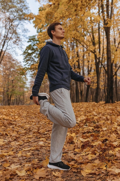 male runner in sportswear stretching legs while standing on pathway in park