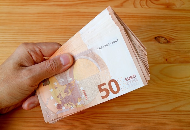 Male's Hand Holding Bundle of 50 EURO Banknotes on Wood