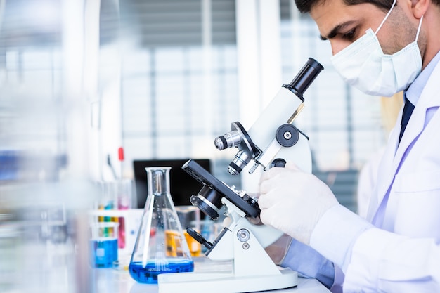 Male scientist looking at Microscope with sample test tube in a chemistry lab