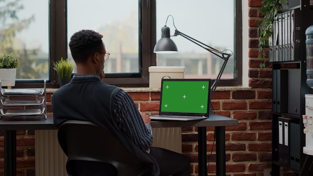 Male secretary analyzing green screen on laptop in startup office. Commercial manager using blank mockup template with isolated chroma key and copy space background on computer display.