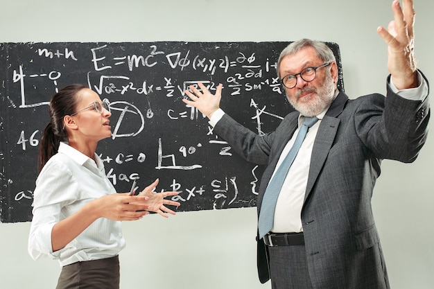 Male senior professor and young female student against chalkboard in classroom. Human emotions concept. Caucasian models. Education, college, university, lecture, school, learning concepts