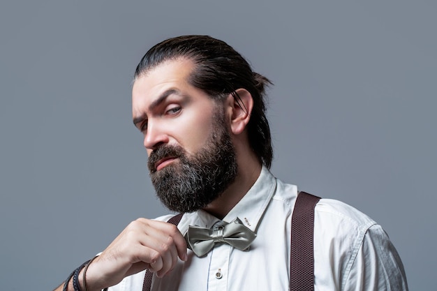 Male in shirt correcting his colorful tie Portrait of handsome bearded man in white shirt and bow tie suspenders Closeup of a gentleman his bowtie Beard man in bow tie and suspenders