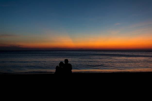 Male silhouette woman sitting hugging at the seaside with twilight