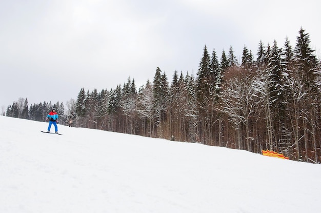 A male snowboarder descends the track next to a snowy forest ski resort winter sport