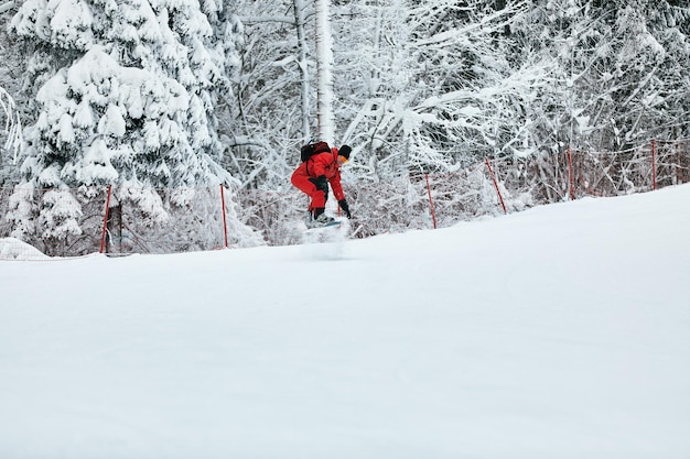 Male snowboarder in a red suit rides on the snowy hill with snowboard Skiing and snowboarding concept