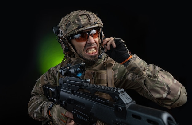 A male soldier in military clothes with a weapon on a dark background