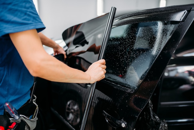 Male specialist applying car tinting film, installation process, tinted auto glass installing procedure