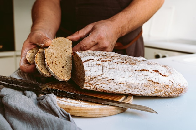 Male strong muscular hands of baker, in flour, cut loaf of craft homemade bread from rye flour