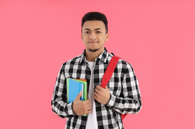 Male student with notebooks and backpack on pink background