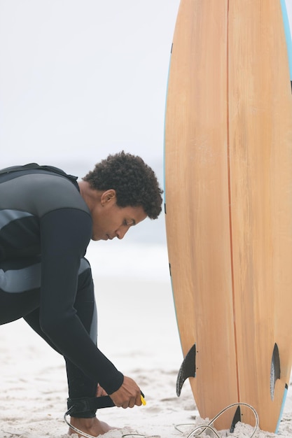 Photo male surfer tying surfboard leash on his leg at beach