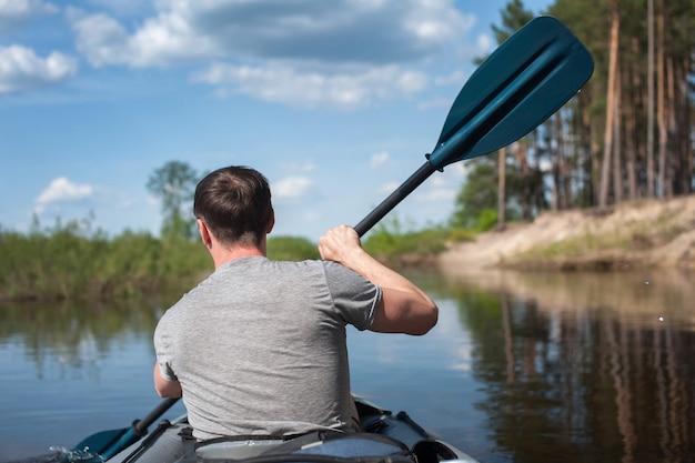 male swims in a kayak in the summer along the river against the backdrop of a pine forest rear view