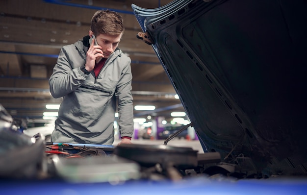 Male talking on phone standing by car with open hood