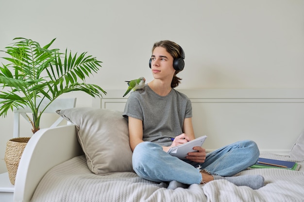 Male teenager with pet green parrot on his shoulder with textbooks