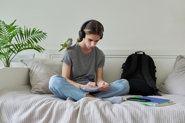 Male teenager with pet parrot guy student sitting in headphones at home