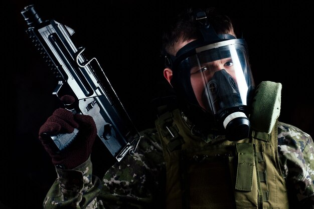 Photo male terrorist in a gas mask holding a gun on a black background.