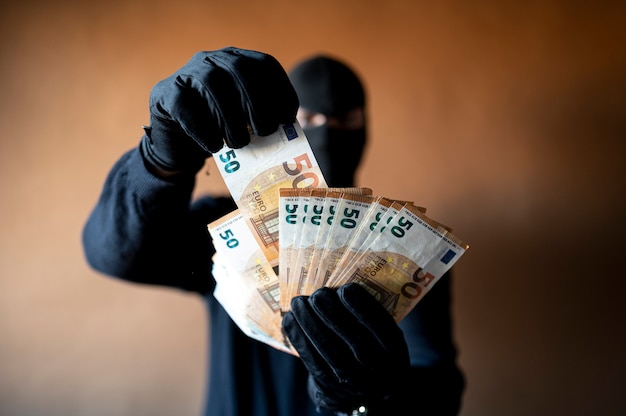 Male thief with balaclava on his head holding a handful of euro bills fanned out