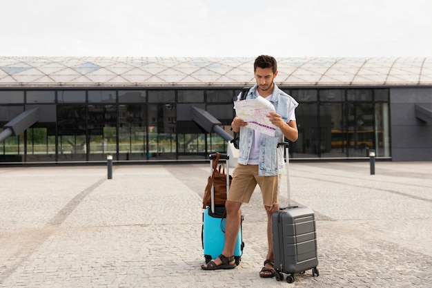 Male tourist stands at the bus station and studies a map of the city