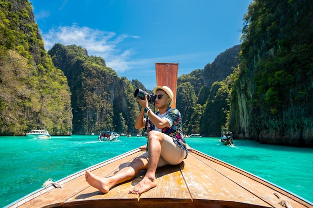 Male tourist taking pictures at the prow of a longtail boat on a tropical island Phi Leh Island