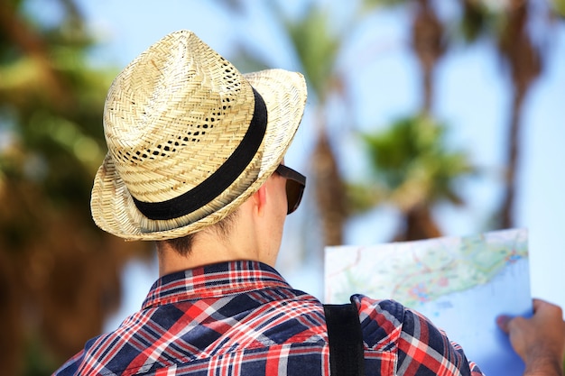 Male tourist with hat looking at map on vacation