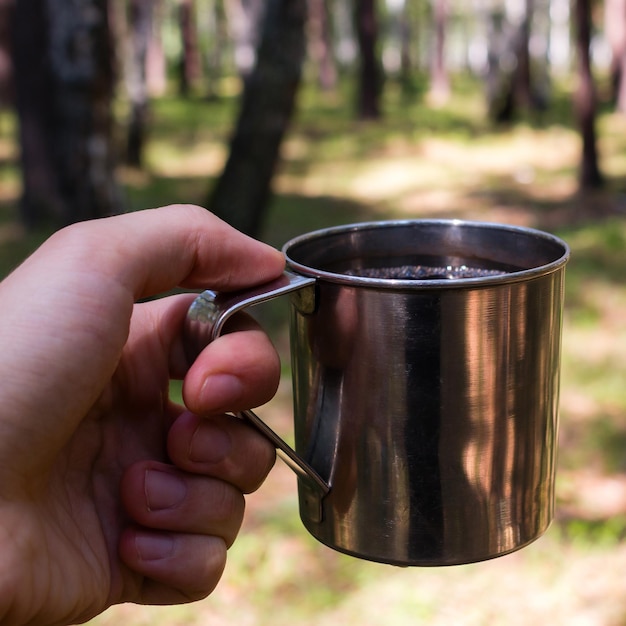 Male traveler holding a mug of tea in the forest