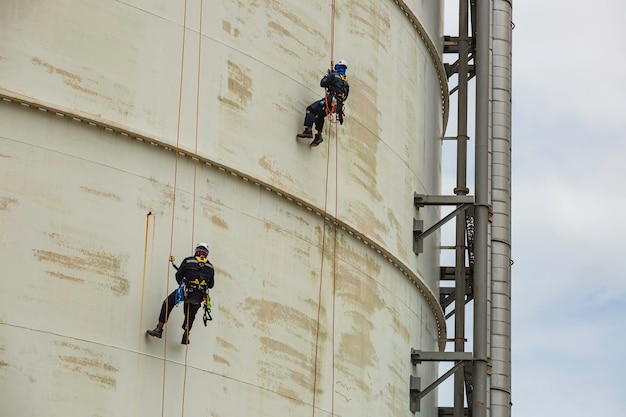 Male two worker inspection wearing safety first harness rope safety line working at a high place on tank roof spherical