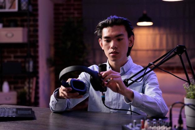 Male vlogger reviewing headphones on livestream, filming podcast video with headset product recommendation. Recording online vlog with sound station and creating social media content.