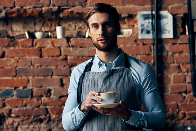 Photo male waiter apron coffee cup brick wall restaurant service high quality photo