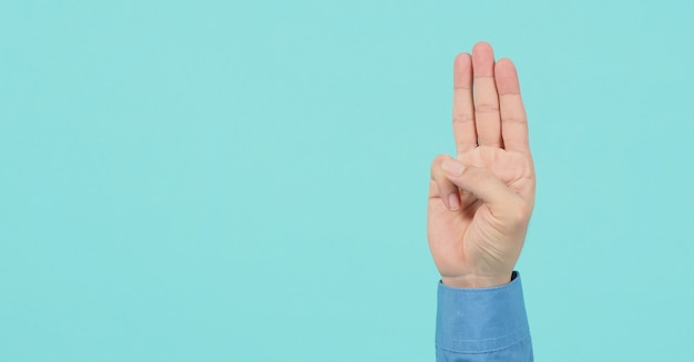 Male wear long sleeve shirt is doing a hand sign of 3 fingers point up meaning three, third or use in protest.It put on blue or green mint backgroud