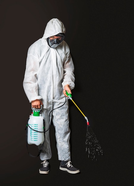 Male wearing protective clothing white sterile uniform with facial mask hand pressure pump disinfecting Worker wearing protective suit using disinfectant manual sprayer isolated on dark background