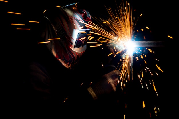 Male welder in a mask performing metal welding. photo in dark colors. sparks flying.