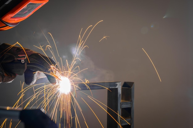 A male welder works at home with a semiautomatic welding machine with golden sparks of steel workpieces Wear a protective mask and wear protective gloves