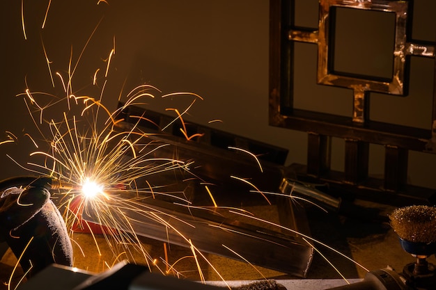 A male welder works at home with a semiautomatic welding machine with golden sparks of steel workpieces Wear a protective mask and wear protective gloves