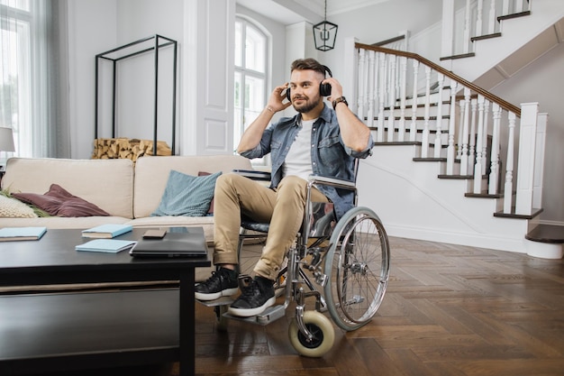 Male wheelchair user with headphones listening songs at home