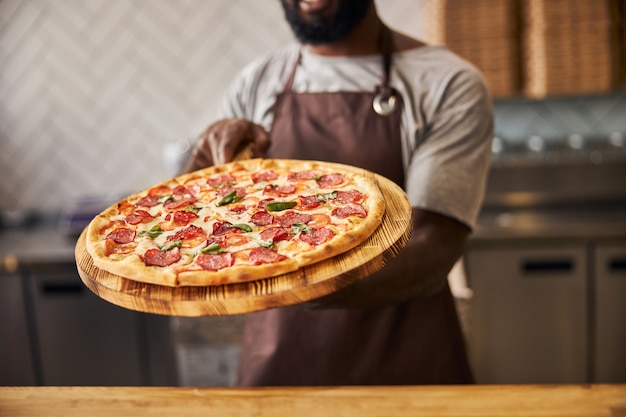 male worker in apron holding delicious pizza with salami, cheese and tomatoes