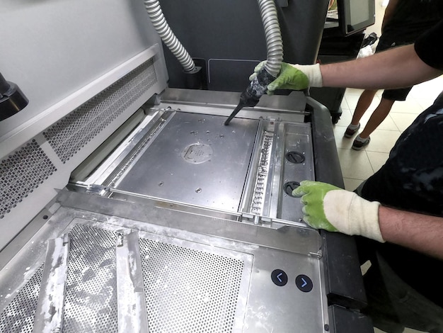 A male worker cleans the surface of an industrial 3D printer from white powder