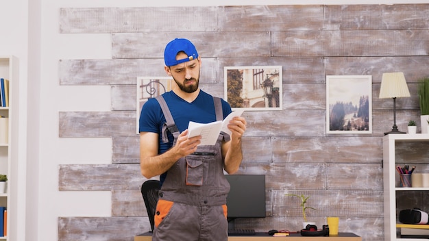 Male worker in coveralls being confused while reading intructions for furniture assembly and leaving from the apartment.