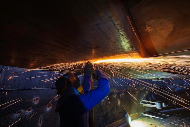 Male worker  grinding on steel plate with flash of sparks close up wear protective gloves oil inside confined spaces.