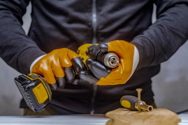 Male worker holds a closeup electric cordless screwdriver in his hands against the background of a construction tool and a concrete wall