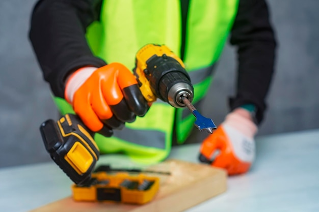 Male worker holds a closeup electric cordless screwdriver in his hands against the background of a construction tool and a concrete wall