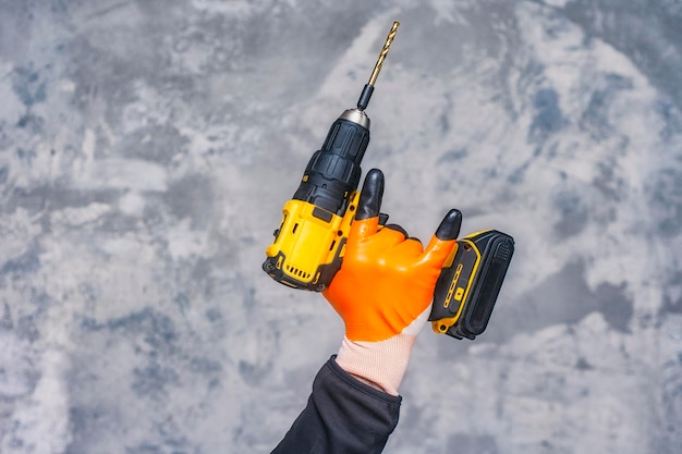 Male worker holds a closeup electric cordless screwdriver in his hands against the background of a construction tool and a concrete wall