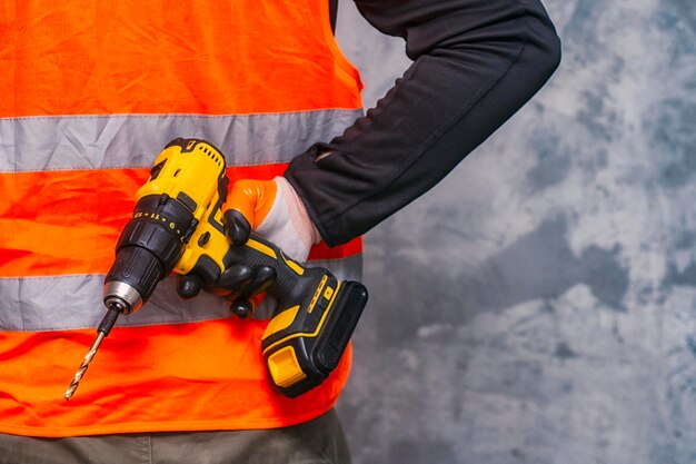 Photo male worker holds a closeup electric cordless screwdriver in his hands against the background of a construction tool and a concrete wall