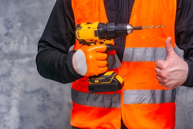 Male worker holds a closeup electric cordless screwdriver in his hands against the background of a construction tool and a concrete wall