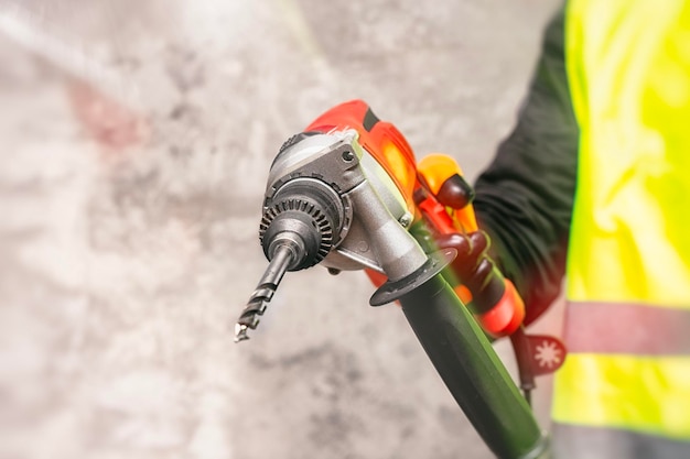 Photo male worker holds a closeup electronic drill in his hands against the background of a concrete wall