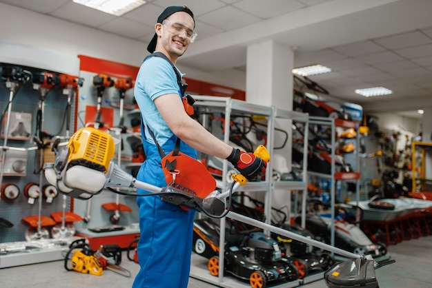 Male worker holds gas trimmer in tool store. Choice of professional equipment in hardware shop, electrical instrument supermarket