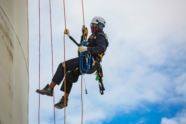 Male worker inspection wearing safety first harness rope safety line working at a high place on tank roof spherical gas blue sky