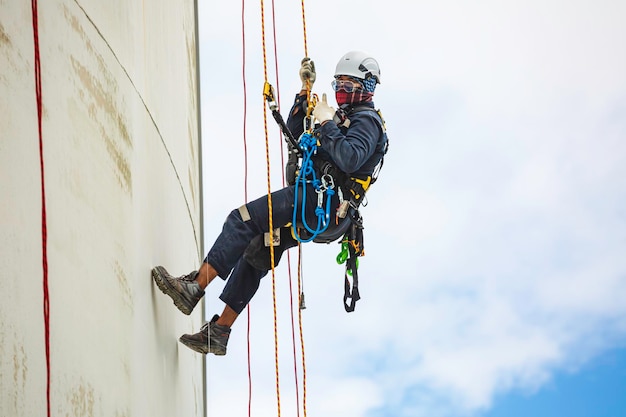 Male worker inspection wearing safety first harness rope safety line working at a high place on tank roof spherical gas blue sky