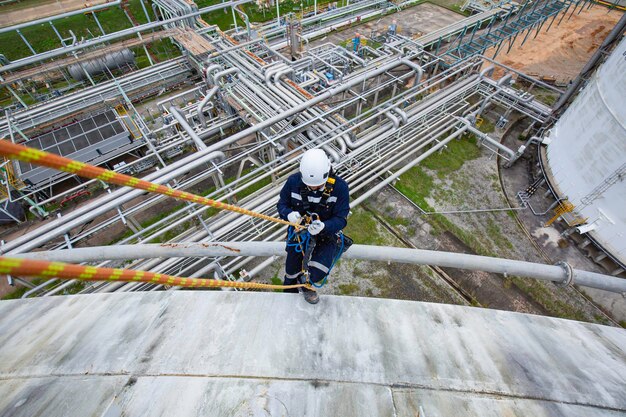 Male worker inspection wearing safety first harness rope safety line working at a high place underside steel long pipes insulation flowing and pipe elbow