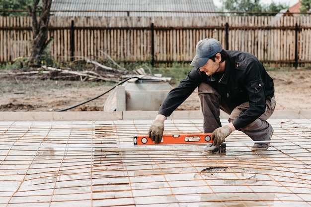 Male worker measures the construction level of rebar for the foundation of a house under construction